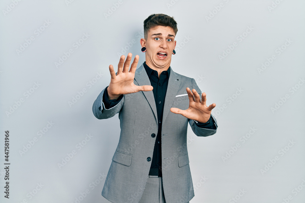 Young caucasian boy with ears dilation wearing business jacket afraid and terrified with fear expression stop gesture with hands, shouting in shock. panic concept. Young caucasian boy with ears dilation wearing business jacket afraid and terrified with fear expression stop gesture with hands, shouting in shock. panic concept.