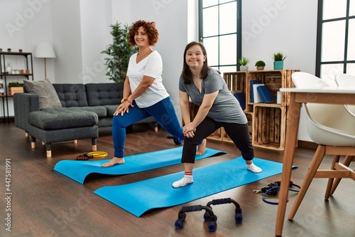 Mature mother and down syndrome daughter doing exercise at home. Stretching at the living room
