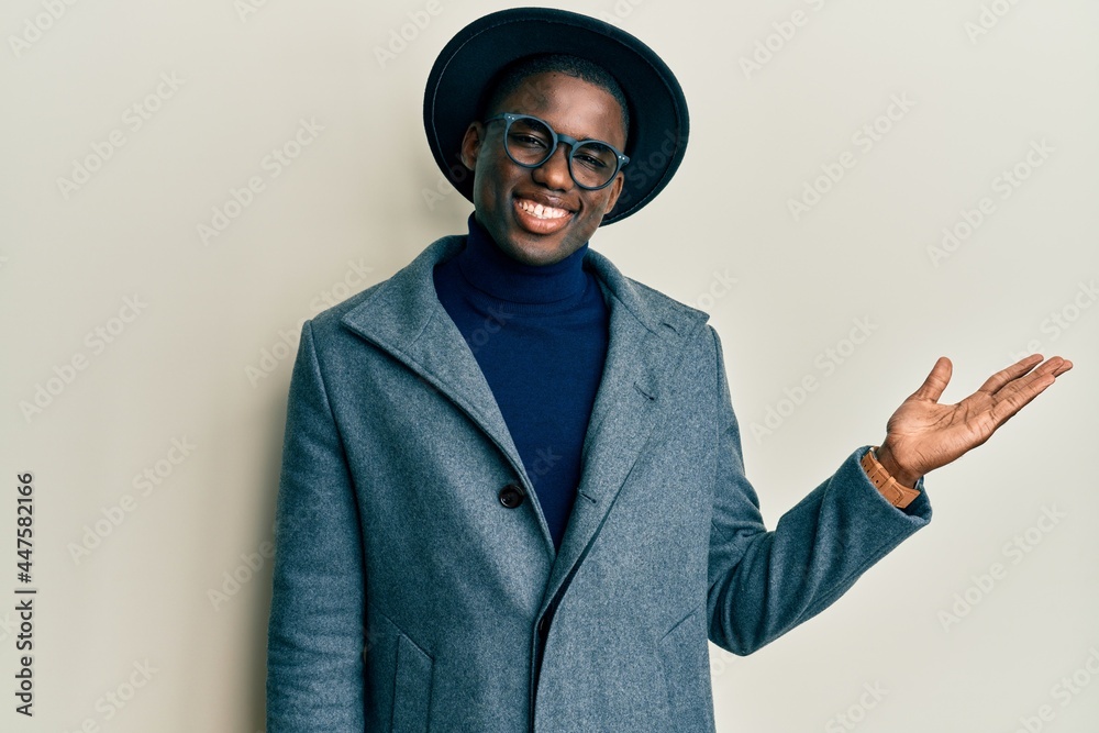 Young african american man wearing elegant style smiling cheerful presenting and pointing with palm of hand looking at the camera. Young african american man wearing elegant style smiling cheerful presenting and pointing with palm of hand looking at the camera.