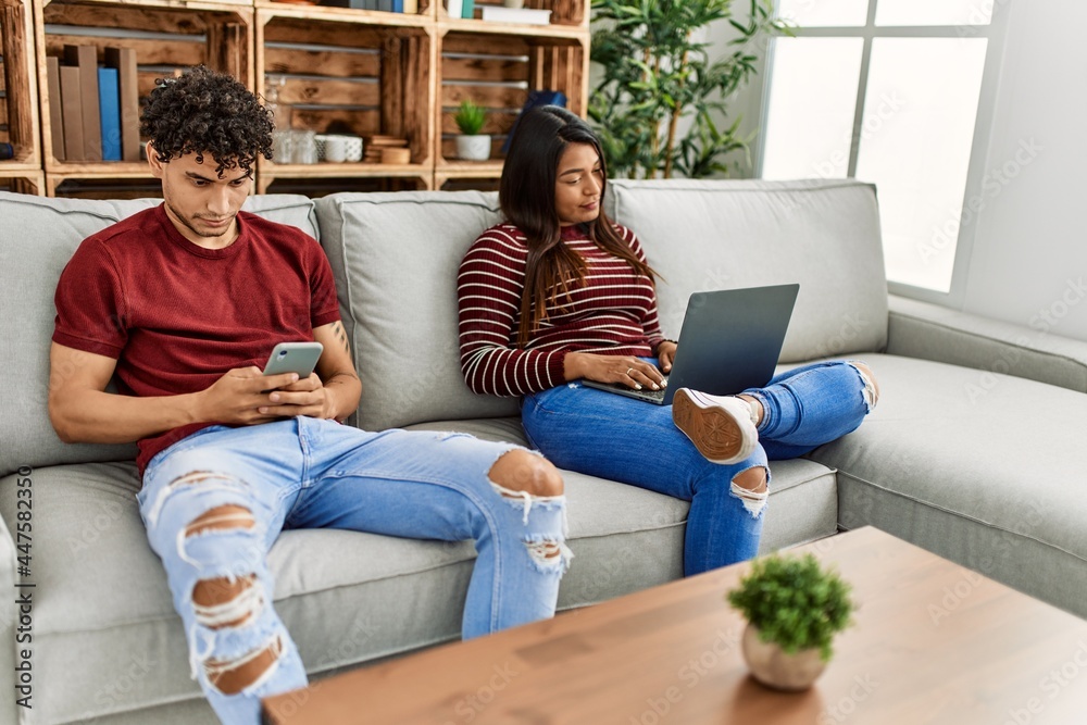 Young latin couple with serious expression using laptop and smartphone at home. Young latin couple with serious expression using laptop and smartphone at home.