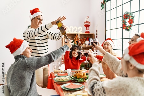 Group of young friends having christmas dinner pouring wine at home.
