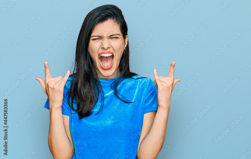 Young hispanic woman wearing casual clothes shouting with crazy expression doing rock symbol with hands up. music star. heavy concept. Young hispanic woman wearing casual clothes shouting with crazy expression doing rock symbol with hands up. music star. heavy concept.