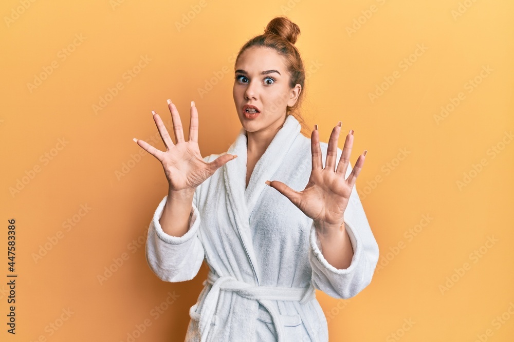 Young blonde woman wearing bathrobe afraid and terrified with fear expression stop gesture with hands, shouting in shock. panic concept. Young blonde woman wearing bathrobe afraid and terrified with fear expression stop gesture with hands, shouting in shock. panic concept.