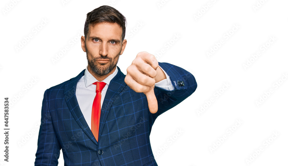 Handsome man with beard wearing business suit and tie looking unhappy and angry showing rejection and negative with thumbs down gesture. bad expression. Handsome man with beard wearing business suit and tie looking unhappy and angry showing rejection and negative with thumbs down gesture. bad expression.