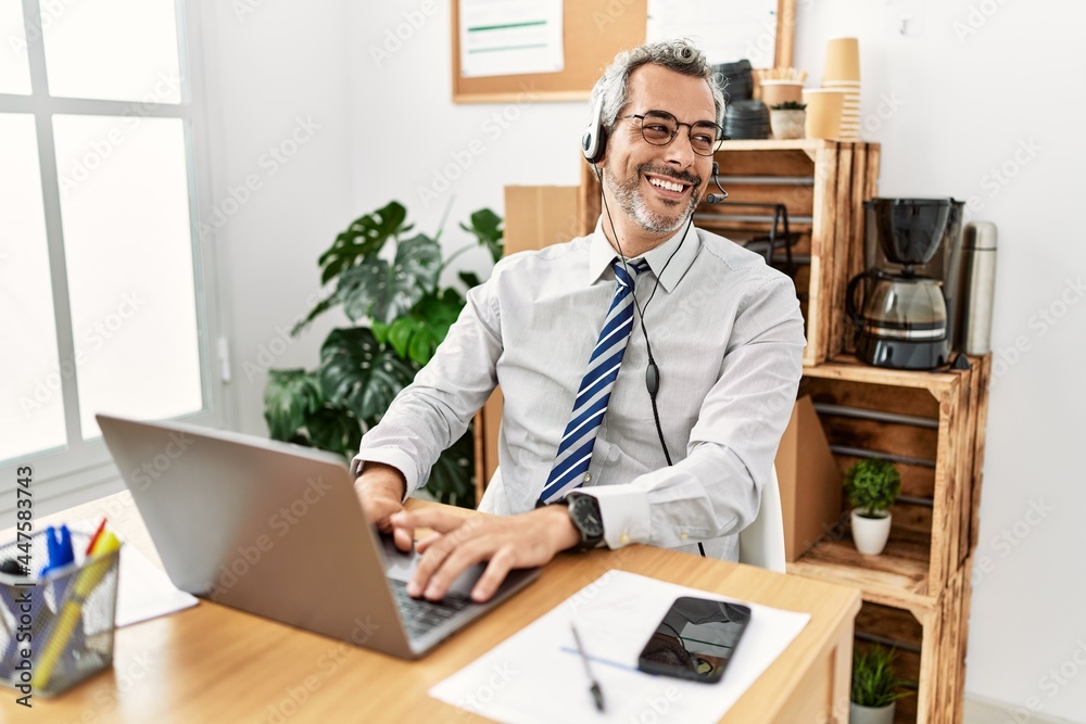 Middle age hispanic business man working at the office wearing operator headset looking away to side with smile on face, natural expression. laughing confident. Middle age hispanic business man working at the office wearing operator headset looking away to side with smile on face, natural expression. laughing confident.