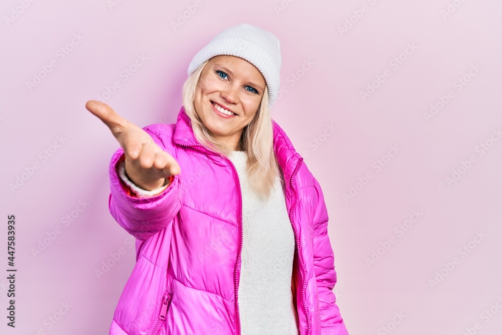 Beautiful caucasian blonde woman wearing wool hat and winter coat smiling friendly offering handshake as greeting and welcoming. successful business. Beautiful caucasian blonde woman wearing wool hat and winter coat smiling friendly offering handshake as greeting and welcoming. successful business.