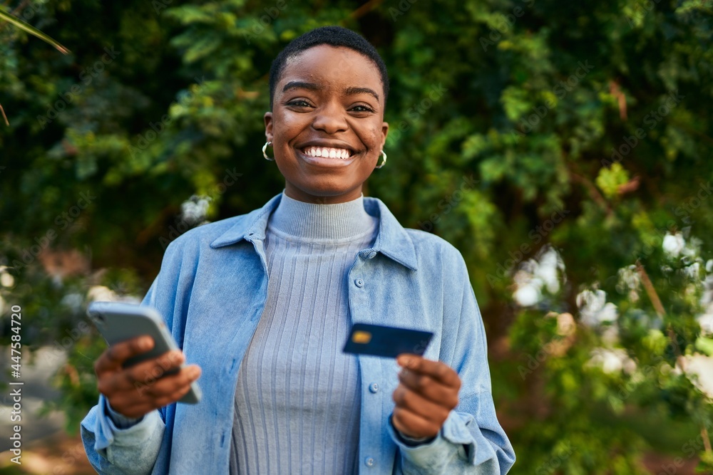 Φωτογραφία Young african american woman smiling happy holding smartphone and credit card at
