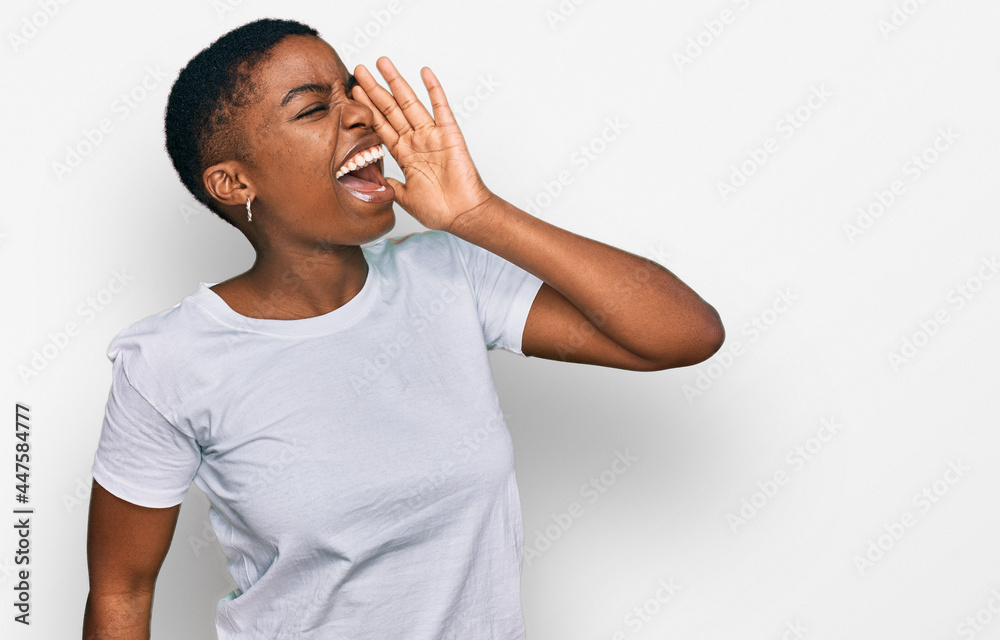 Young african american woman wearing casual white t shirt shouting and screaming loud to side with hand on mouth. communication concept. Young african american woman wearing casual white t shirt shouting and screaming loud to side with hand on mouth. communication concept.