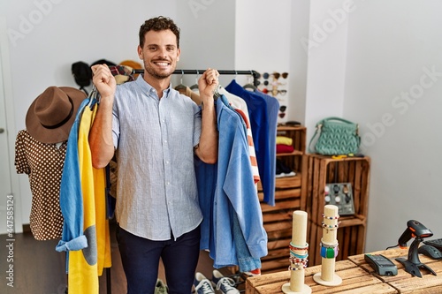 Young hispanic customer man smiling happy holding clothes at clothing store.