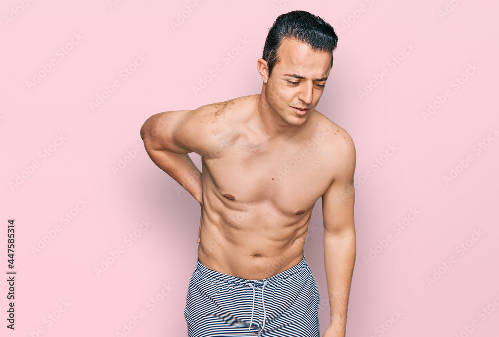 Fototapeta premium Handsome young man wearing swimwear shirtless suffering of backache, touching back with hand, muscular pain