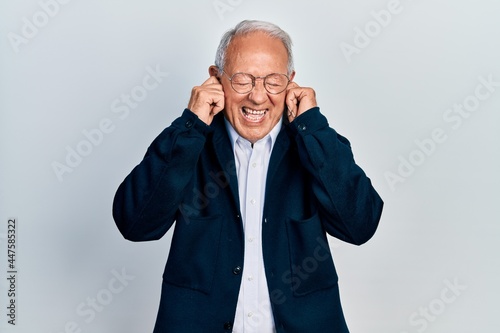 Senior man with grey hair wearing casual style and glasses covering ears with fingers with annoyed expression for the noise of loud music. deaf concept.