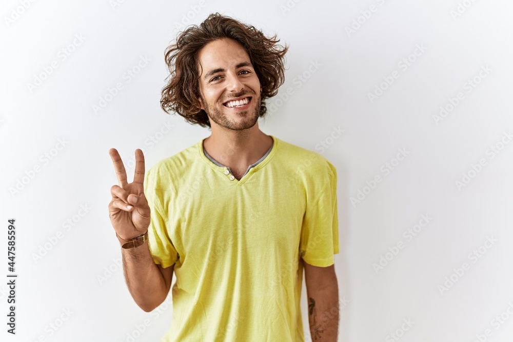 Young hispanic man standing over isolated background showing and pointing up with fingers number two while smiling confident and happy. Young hispanic man standing over isolated background showing and pointing up with fingers number two while smiling confident and happy.