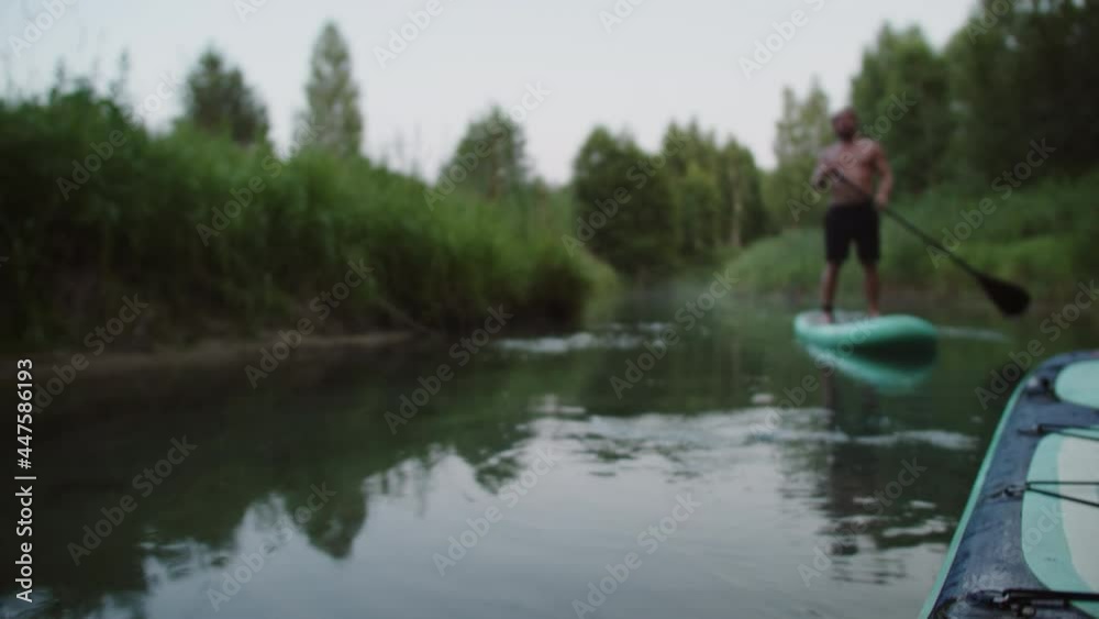 Surfer brutal man standing on surfing board and paddling in river close-up. Sportsman surfing alone, training. Male coach rowing while swimming on surfboard. Sport and nature concept, extreme. Surfer brutal man standing on surfing board and paddling in river close-up. Sportsman surfing alone, training. Male coach rowing while swimming on surfboard. Sport and nature concept, extreme.