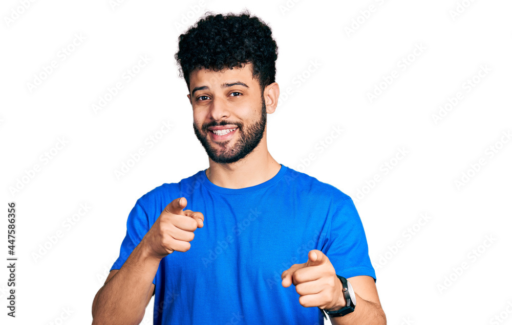 Young arab man with beard wearing casual blue t shirt pointing fingers to camera with happy and funny face. good energy and vibes. Young arab man with beard wearing casual blue t shirt pointing fingers to camera with happy and funny face. good energy and vibes.