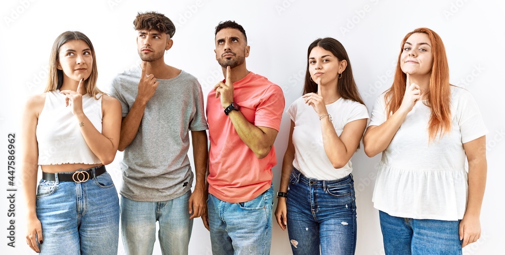 Obraz premium Group of young friends standing together over isolated background thinking concentrated about doubt with finger on chin and looking up wondering