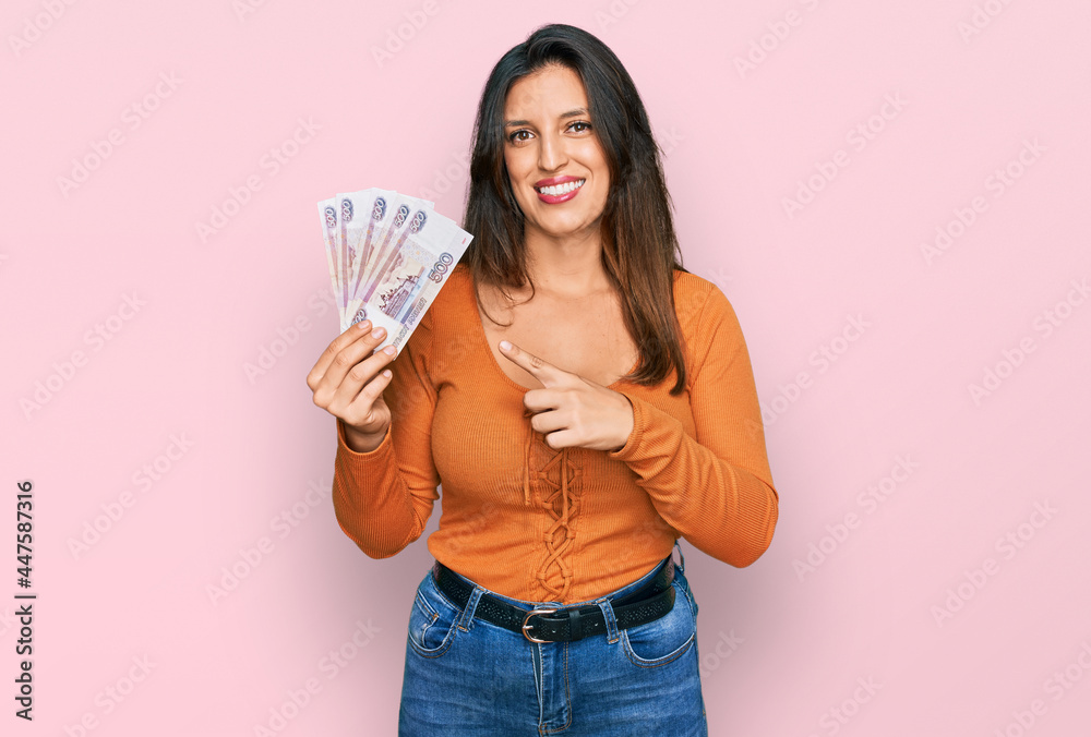 Beautiful hispanic woman holding russian 500 ruble banknotes smiling happy pointing with hand and finger Beautiful hispanic woman holding russian 500 ruble banknotes smiling happy pointing with hand and finger