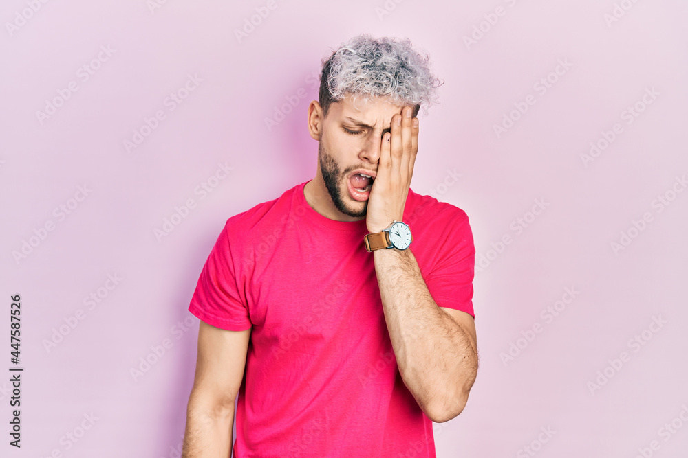 Young hispanic man with modern dyed hair wearing casual pink t shirt yawning tired covering half face, eye and mouth with hand. face hurts in pain. Young hispanic man with modern dyed hair wearing casual pink t shirt yawning tired covering half face, eye and mouth with hand. face hurts in pain.
