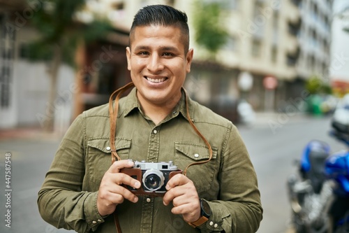 Young latin tourist man smiling happy using vintage camera at the city.