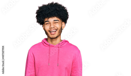 Young african american man with afro hair wearing casual pink sweatshirt winking looking at the camera with sexy expression, cheerful and happy face.
