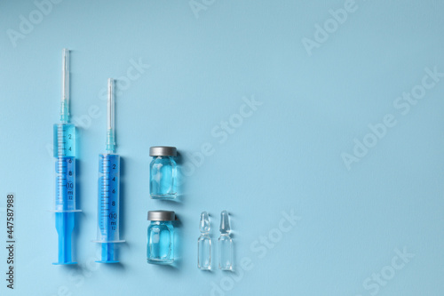 Disposable syringes with needles  ampules and vials on light blue background  flat lay. Space for text
