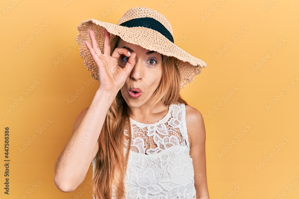 Young caucasian woman wearing summer hat doing ok gesture shocked with surprised face, eye looking through fingers. unbelieving expression. Young caucasian woman wearing summer hat doing ok gesture shocked with surprised face, eye looking through fingers. unbelieving expression.