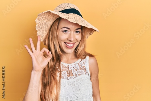 Young caucasian woman wearing summer hat smiling positive doing ok sign with hand and fingers. successful expression.