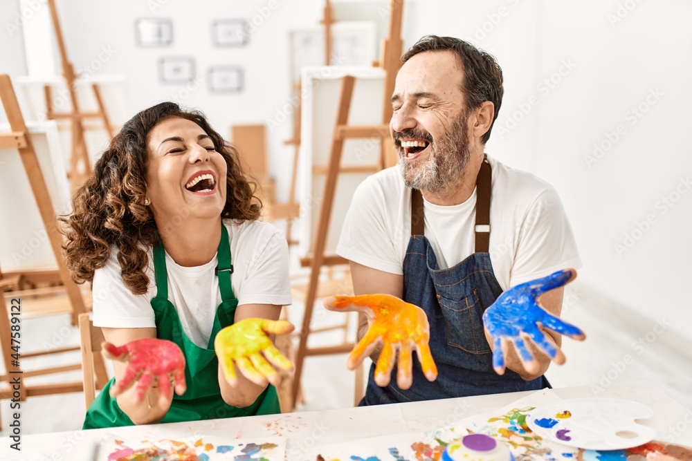 Two middle age student smiling happy showing paint hands at art studio.