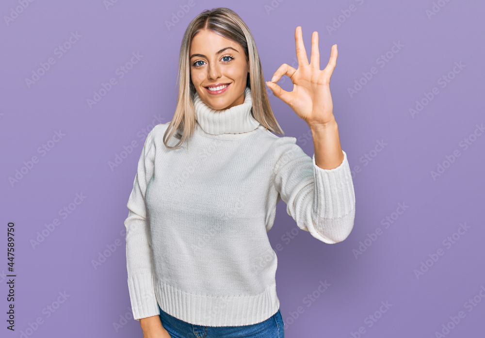 Beautiful blonde woman wearing casual turtleneck sweater smiling positive doing ok sign with hand and fingers. successful expression. Beautiful blonde woman wearing casual turtleneck sweater smiling positive doing ok sign with hand and fingers. successful expression.