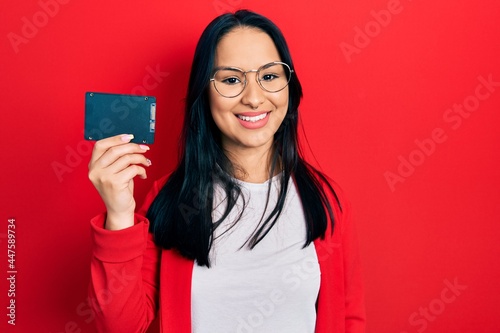 Beautiful hispanic woman with nose piercing holding ssd memory looking positive and happy standing and smiling with a confident smile showing teeth