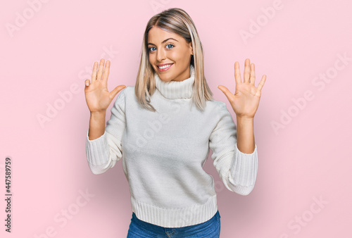 Beautiful blonde woman wearing casual turtleneck sweater showing and pointing up with fingers number nine while smiling confident and happy.