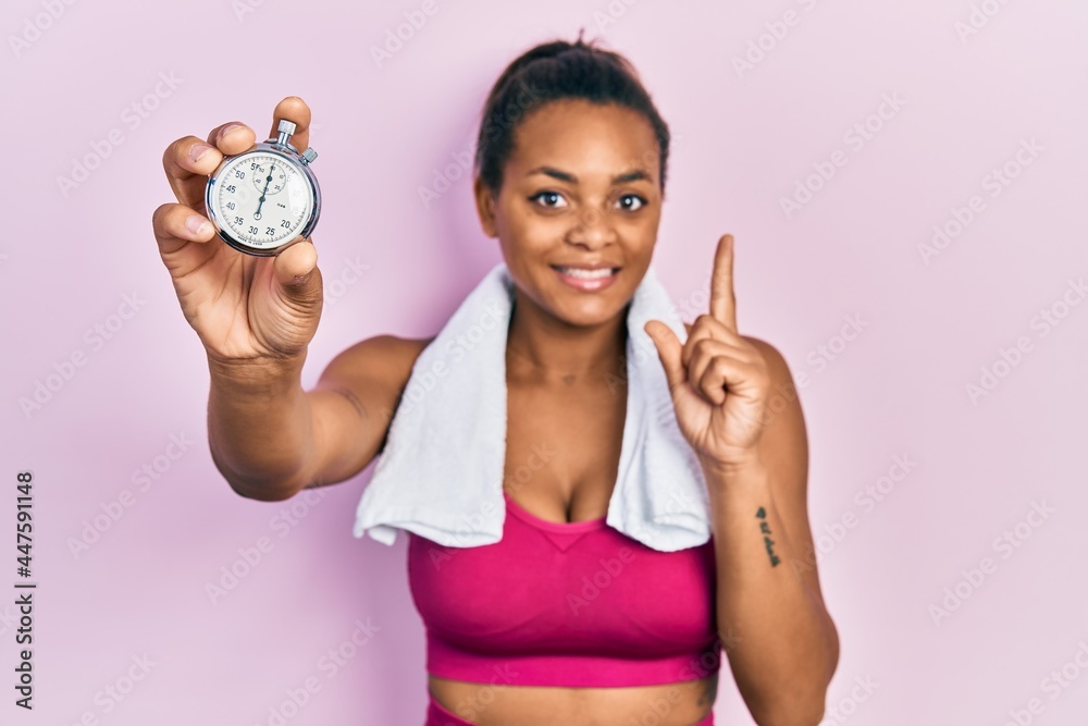 Young african american girl wearing sportswear holding stopwatch smiling with an idea or question pointing finger with happy face, number one Young african american girl wearing sportswear holding stopwatch smiling with an idea or question pointing finger with happy face, number one