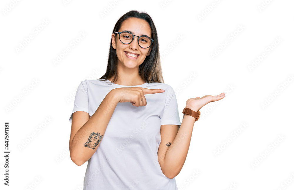 Young hispanic woman wearing casual white t shirt amazed and smiling to the camera while presenting with hand and pointing with finger. Young hispanic woman wearing casual white t shirt amazed and smiling to the camera while presenting with hand and pointing with finger.