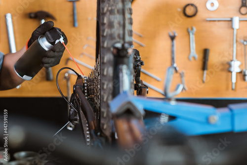 close up of a mechanic's hand wearing gloves using chain lube lubricating the chain and freewheel on a workshop background photo