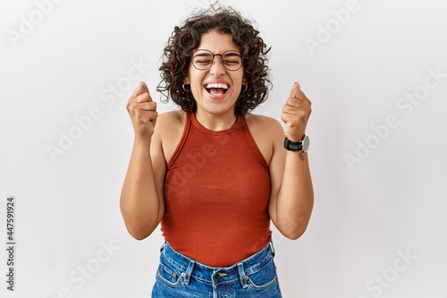 Young hispanic woman wearing glasses standing over isolated background excited for success with arms raised and eyes closed celebrating victory smiling. winner concept.