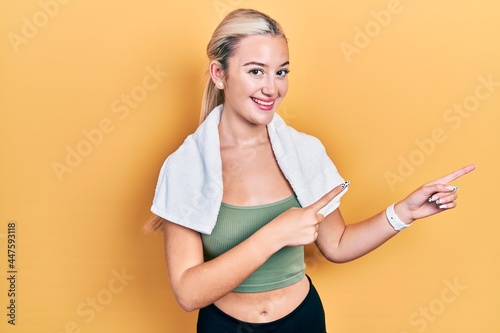 Young blonde girl wearing sportswear and towel smiling and looking at the camera pointing with two hands and fingers to the side. © Krakenimages.com