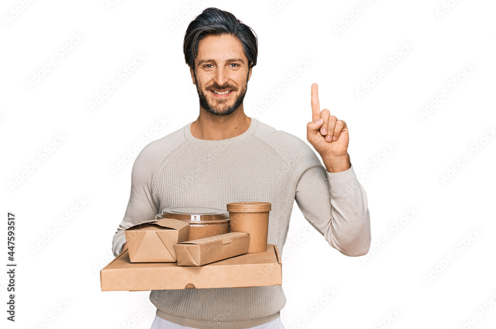 Young hispanic man holding take away food surprised with an idea or question pointing finger with happy face, number one Young hispanic man holding take away food surprised with an idea or question pointing finger with happy face, number one