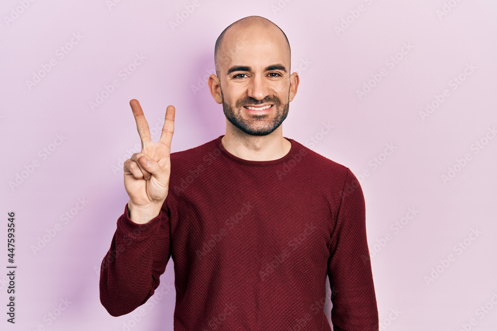 Young bald man wearing casual clothes showing and pointing up with fingers number two while smiling confident and happy. Young bald man wearing casual clothes showing and pointing up with fingers number two while smiling confident and happy.