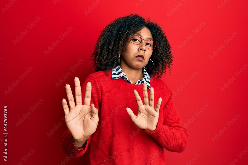 Beautiful african american woman with afro hair wearing sweater and glasses moving away hands palms showing refusal and denial with afraid and disgusting expression. stop and forbidden. Beautiful african american woman with afro hair wearing sweater and glasses moving away hands palms showing refusal and denial with afraid and disgusting expression. stop and forbidden.