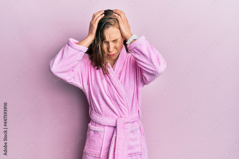 Young blonde woman wearing bathrobe suffering from headache desperate and stressed because pain and migraine. hands on head. Young blonde woman wearing bathrobe suffering from headache desperate and stressed because pain and migraine. hands on head.