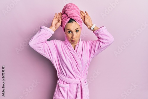 Young blonde woman wearing shower towel cap and bathrobe doing bunny ears gesture with hands palms looking cynical and skeptical. easter rabbit concept. © Krakenimages.com