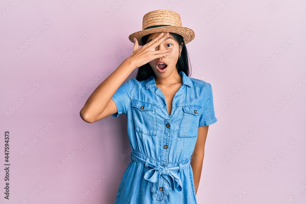 Young chinese woman wearing summer hat peeking in shock covering face and eyes with hand, looking through fingers afraid Young chinese woman wearing summer hat peeking in shock covering face and eyes with hand, looking through fingers afraid