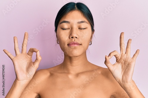 Obraz na plátně Young chinese woman standing topless showing skin relax and smiling with eyes closed doing meditation gesture with fingers