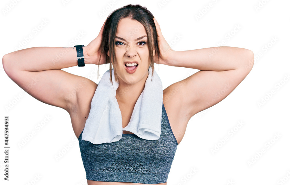 Young hispanic girl wearing sportswear and towel crazy and scared with hands on head, afraid and surprised of shock with open mouth Young hispanic girl wearing sportswear and towel crazy and scared with hands on head, afraid and surprised of shock with open mouth
