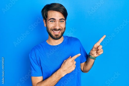 Young hispanic man wearing casual clothes smiling and looking at the camera pointing with two hands and fingers to the side.