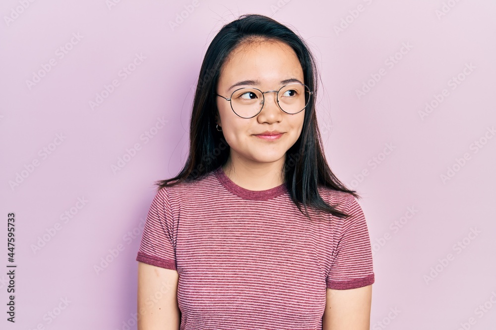 Young chinese girl wearing casual clothes and glasses smiling looking to the side and staring away thinking. Young chinese girl wearing casual clothes and glasses smiling looking to the side and staring away thinking.