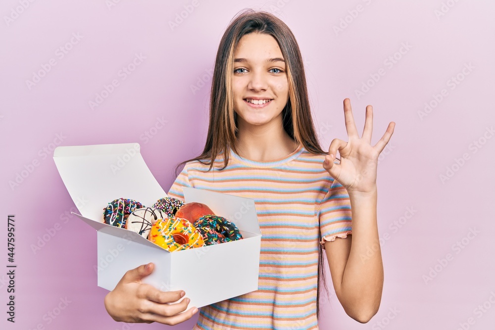Young brunette girl holding tasty colorful doughnuts doing ok sign with fingers, smiling friendly gesturing excellent symbol Young brunette girl holding tasty colorful doughnuts doing ok sign with fingers, smiling friendly gesturing excellent symbol