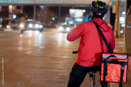 Stock photo of a food deliveryman in red uniform carrying a food delivery box to deliver for customer for order during COVID-19 pandemic and lockdown in the city at night time in Thailand.