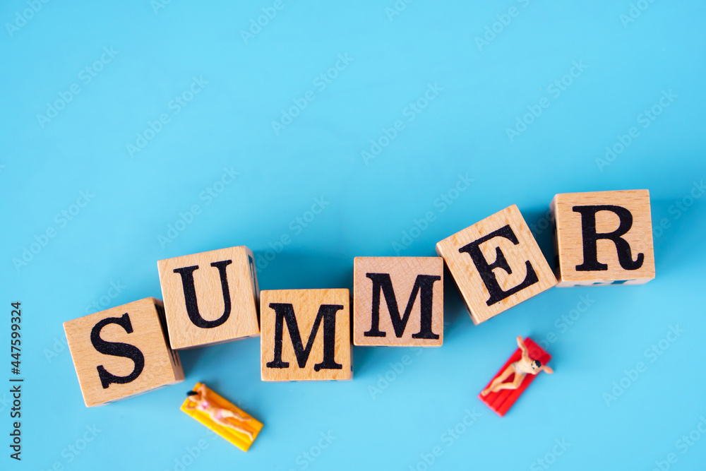 Obraz premium Summer concept : Minature people are taking sun bath on the SUMMER Word written on wooden cubes and a blue background.