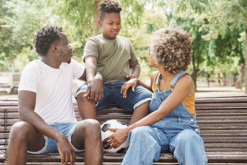 African American family with young cool millennial parents and cute kid sitting on bench in outdoor public park © EFStock