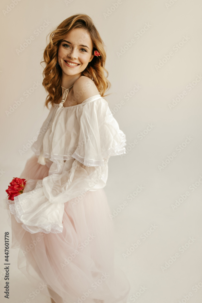 Wonderful young woman with curly hair in white shirt and pink long skirt looking into camera and smiling in isolated backdrop.. Wonderful young woman with curly hair in white shirt and pink long skirt looking into camera and smiling in isolated backdrop..